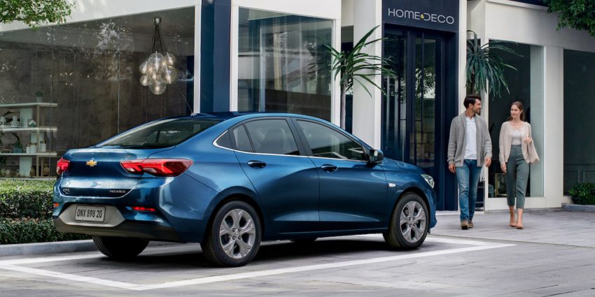 Chevrolet Onix Plus azul em frente a uma loja decoração com um casa indo até o carro